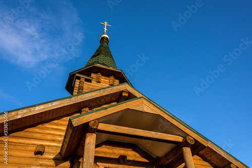 Russia, Karelia, White Sea, near Kem: Old wooden chapel church in warm late afternoon sunlight with golden orthodox cross and blue sky in the background - concept religion Christianity architecture photo