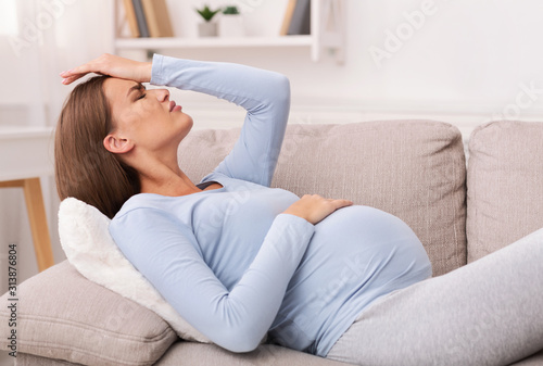 Pregnant Woman Touching Forehead Having Migraine Lying On Sofa