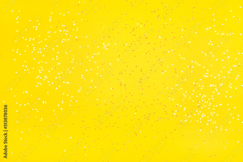 Tiny pearl stars on yellow background. Flat lay, top view.