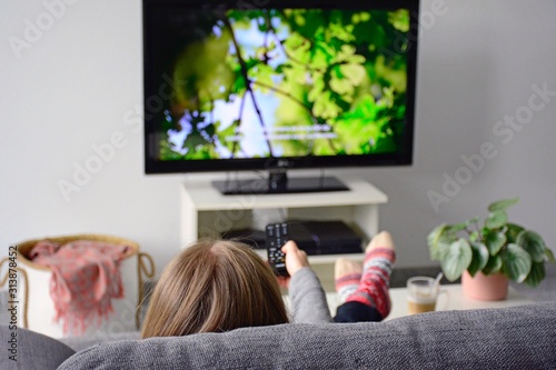Young woman watching television with subtitles while sitting comfortably on sofa at home in living room. Nature, green, documentary, tv screen photo