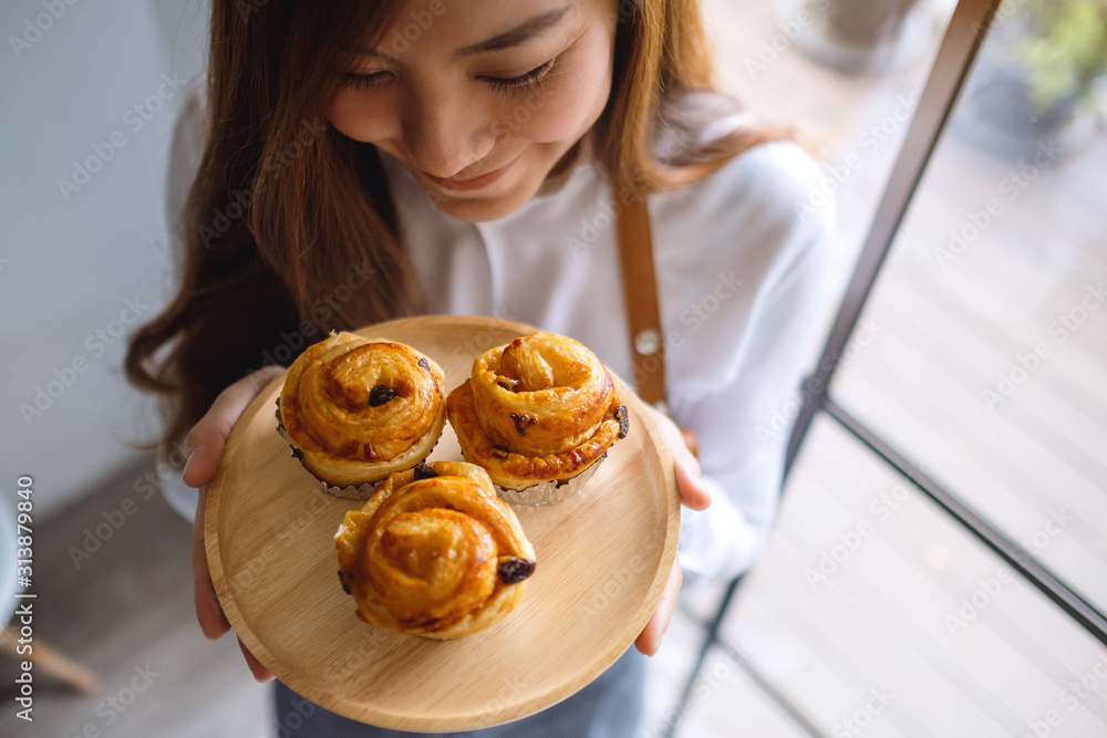 Top view image of a waitress holding and smelling raisin danish in wooden plate Top view image of a waitress holding and smelling raisin danish in wooden plate