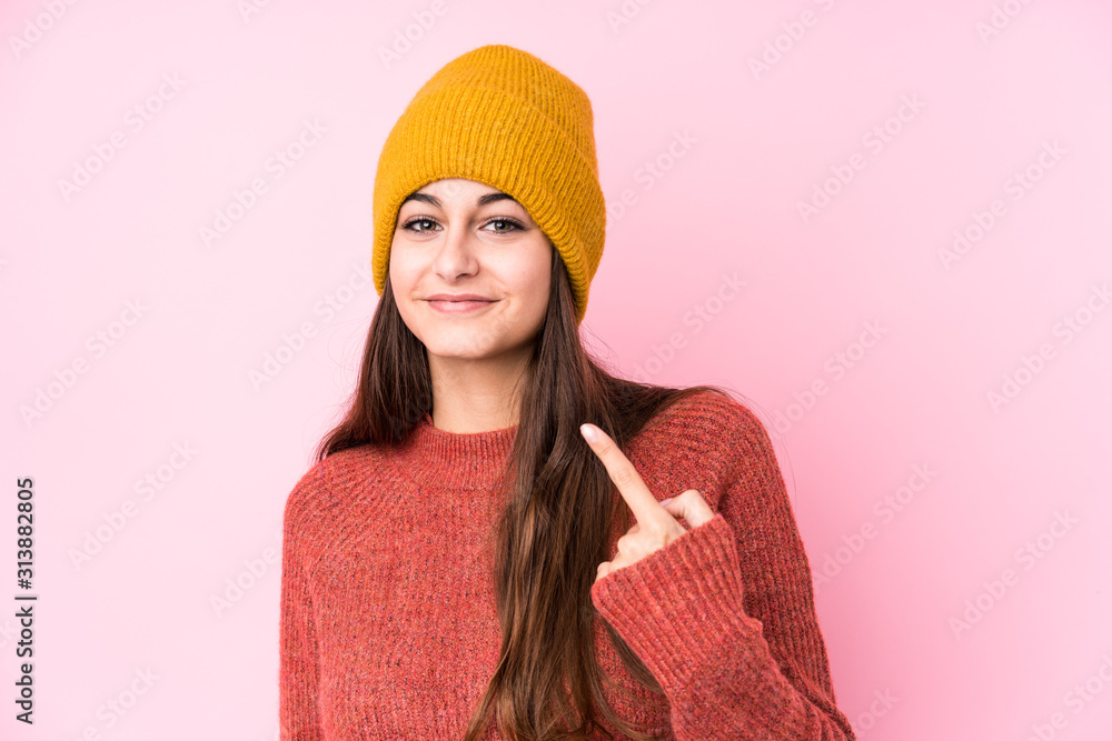 Young caucasian woman wearing a wool cap pointing with finger at you as if inviting come closer. Young caucasian woman wearing a wool cap pointing with finger at you as if inviting come closer.