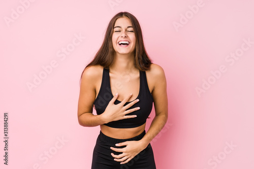 Young caucasian fitness woman doing sport isolated laughs happily and has fun keeping hands on stomach.