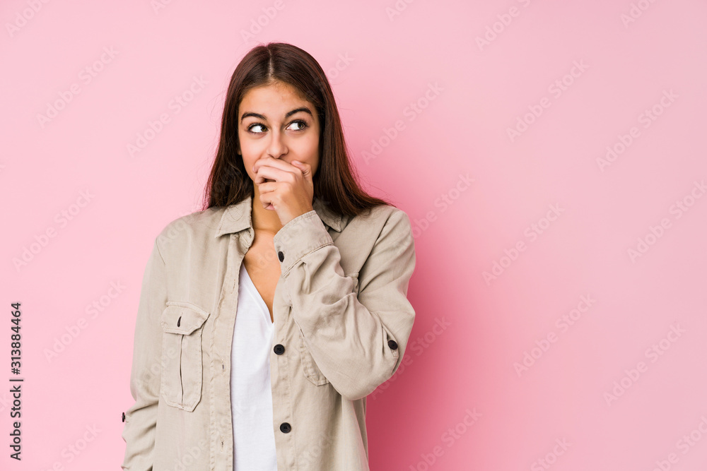 Young caucasian woman posing in a pink background thoughtful looking to a copy space covering mouth with hand. Young caucasian woman posing in a pink background thoughtful looking to a copy space covering mouth with hand.
