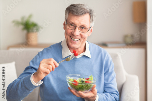 Senior Man Eating Vegetable Salad Sitting On Couch At Home