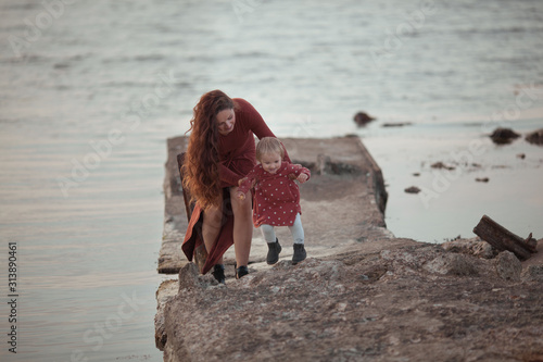 A little girl and mom walk near the sea, they play and hug