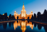 Moscow State University in golden light against a blue sky with reflections in the water