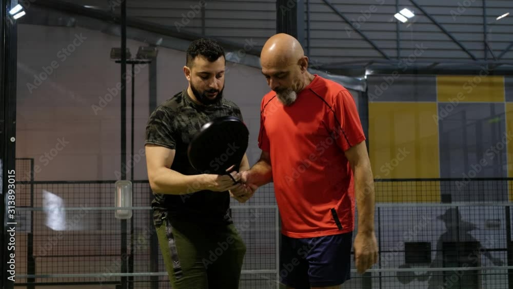 Son teaches his father how to perform a tennis paddle kick and how to position himself Son teaches his father how to perform a tennis paddle kick and how to position himself