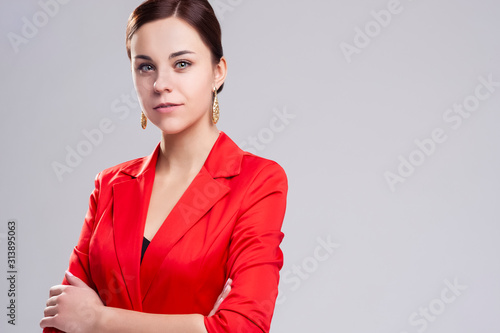 Portrait of Smiling Fashionable Caucasian Woman in Red Blazer Posing Against Gray in Studio. photo