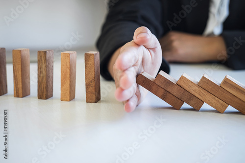 Risk and Strategy in Business, Image of hand stopping falling collapse wooden block dominoes effect from continuous toppled block, prevention and development to stability