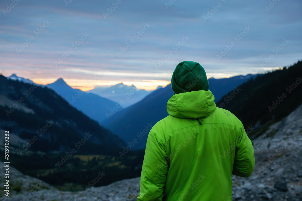 Adventurous man with green jacket is enjoying the beautiful natural view of the Canadian Mountain Landscape during cloudy sunset. Taken near Chilliwack, East of Vancouver, BC, Canada.