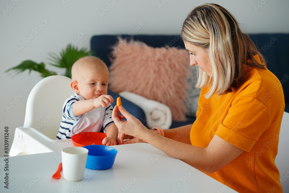 Mom feeding her baby girl with a spoon. Mother giving food to her eight-month child at home.