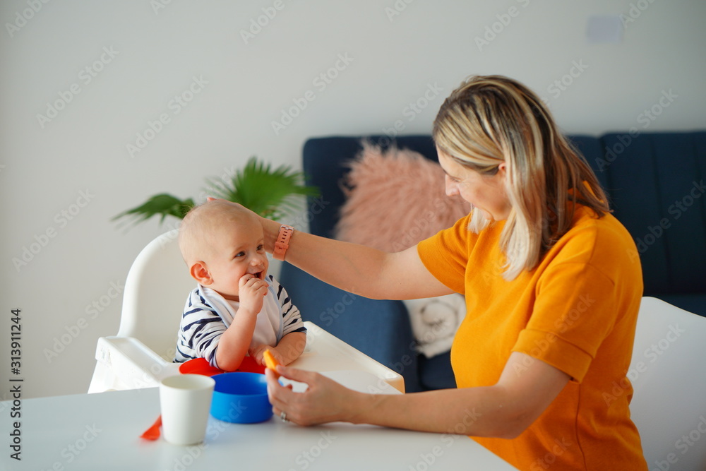 Mom feeding her baby girl with a spoon. Mother giving food to her eight-month child at home.