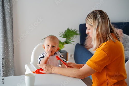 Obraz na płótnie Mom feeding her baby girl with a spoon. Mother giving food to her eight-month child at home. w salonie