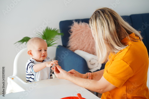 Mom feeding her baby girl with a spoon. Mother giving food to her eight-month child at home.