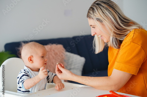 Mom feeding her baby girl with a spoon. Mother giving food to her eight-month child at home.