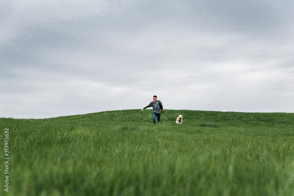 Teenage boy running across a grassy field with his dog on cloudy day. Teenage boy running across a grassy field with his dog on cloudy day.