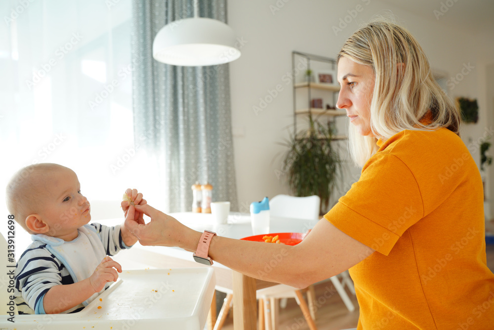 Mom feeding her baby girl with a spoon. Mother giving food to her eight-month child at home.