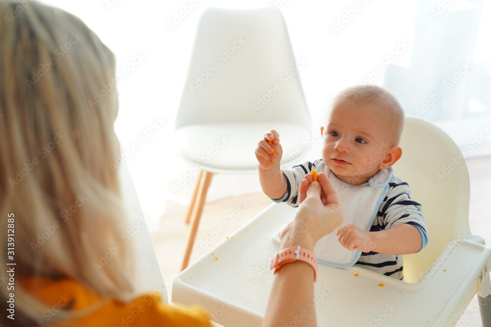 Mom feeding her baby girl with a spoon. Mother giving food to her eight-month child at home.