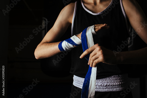 Young boxer placing hand bandages in gym before training. photo