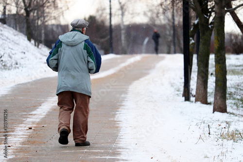 Fotografi Elderly man walking on the rural street during a snow