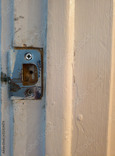 Old rusty door catch on a white wall.