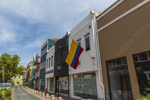 Beautiful landscape view of central street of city Willemstad, Curacao. Colorful buildings Embassy of Colombia and green trees on blue sky with white clouds background. 