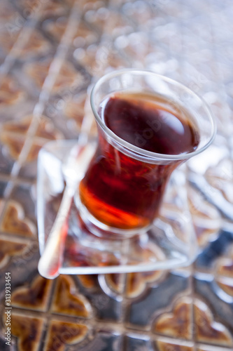 Shiny glass of hot black Turkish tea sitting on textured traditional tile table
