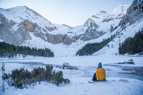 Girl sitting on the shore of an icy mountain lake.