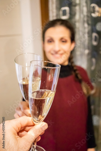 People having fun together toasting drinks in the home kitchen. Happy and smiling woman toasts with flute of sparkling wine (champagne). Focus on central glass. Friendship, love and family concept.