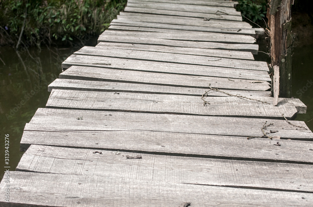 Small weathered wooden boards bridge over river waters closeup Small weathered wooden boards bridge over river waters closeup