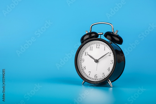 Retro alarm clock on blue background. Retro black vintage alarm clock on blue background