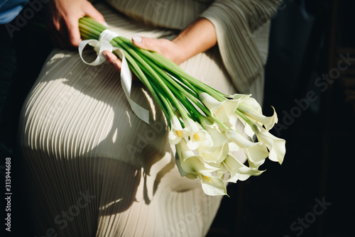 Woman in pastel or ivory dress holding a beautiful bouquet of calla lily flowers