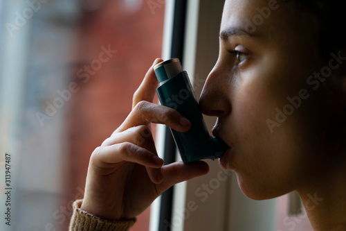 Young woman taking the blue asthma inhaler to treat an asthma attack. photo