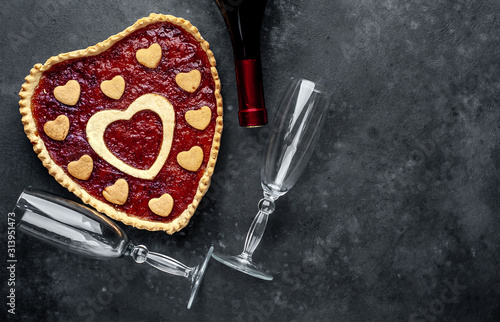 heart-shaped cake with jam, a bottle of wine and glasses, on a stone background with copy space for your text. valentine's day celebration concept