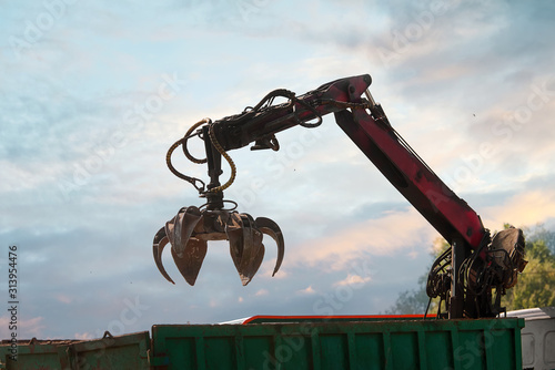 Grapple truck unloads scrap industrial metal for recycling. Manipulator with hydraulic magnet crab against sky.  Crane garbage truck loading industry waste. Crane grab scrap..