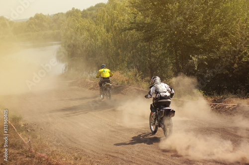 Two motorcyclists catching up with each other in the dust, view from the back, motocross sport competition