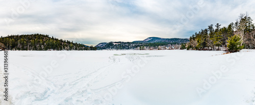 A view across frozen Crystal Lake, New Hampshire under cloudy sky towards trees and mountains in the distance.