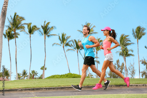 Healthy couple running together happy partner workout training outdoors in tropical city background. Woman and man jogging outside.