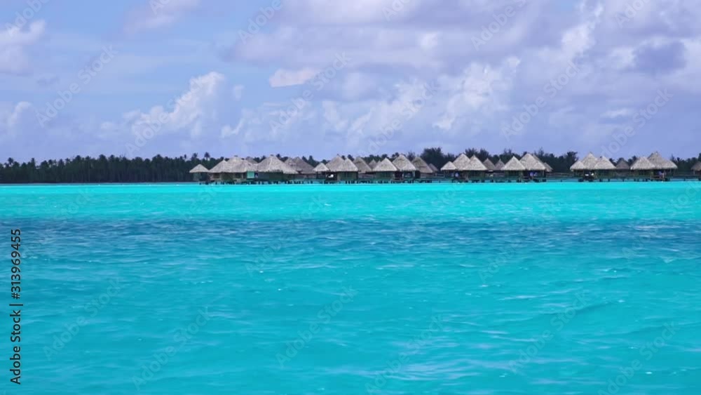 Low angle aerial glide view of overwater bungalow villas in turquoise lagoon. Bora Bora, Tahiti French Polynesia. Luxury honeymoon vacation, romantic getaway, exotic resort destination. Low angle aerial glide view of overwater bungalow villas in turquoise lagoon. Bora Bora, Tahiti French Polynesia. Luxury honeymoon vacation, romantic getaway, exotic resort destination.