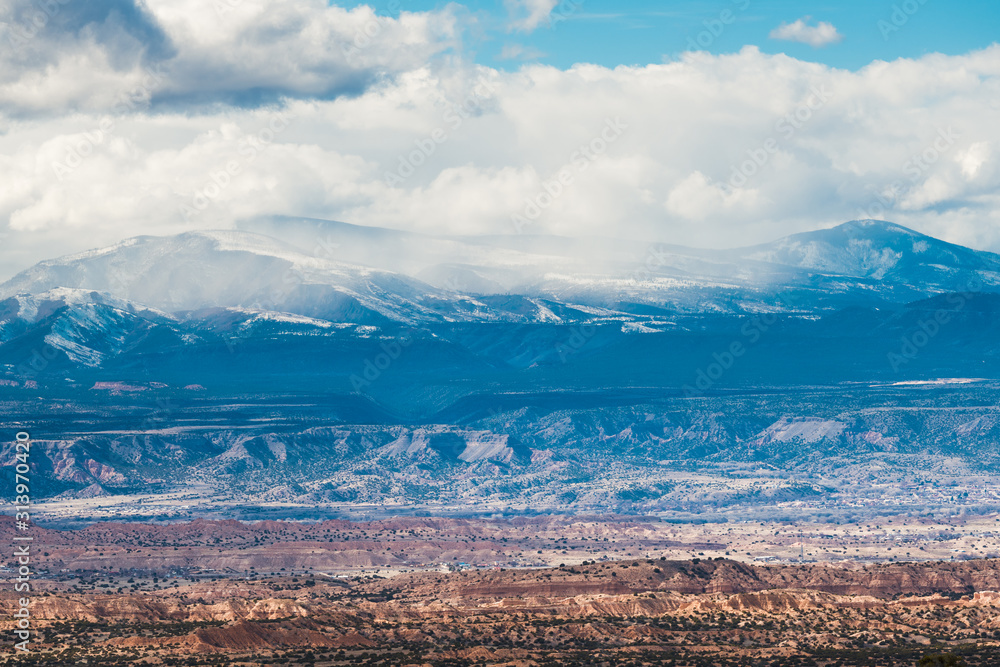 Naklejka premium A vast colorful desert landscape under snow-capped mountains and winter storm clouds
