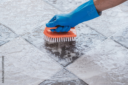 Hand of man wearing blue rubber gloves is used to convert scrub cleaning on the tile floor.