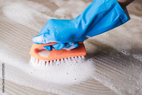 Hand of man wearing blue rubber gloves is used to convert scrub cleaning on the tile floor.