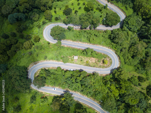 Aerial view of curve road cut throug the green forest in the highland mountains in Chiang Rai province, Thailand. The highland of Chiang Rai is a popular destination during the cold weather season.