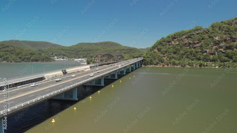 Aerial panning shot of cars driving along a highway bridge above a river. Aerial panning shot of cars driving along a highway bridge above a river.