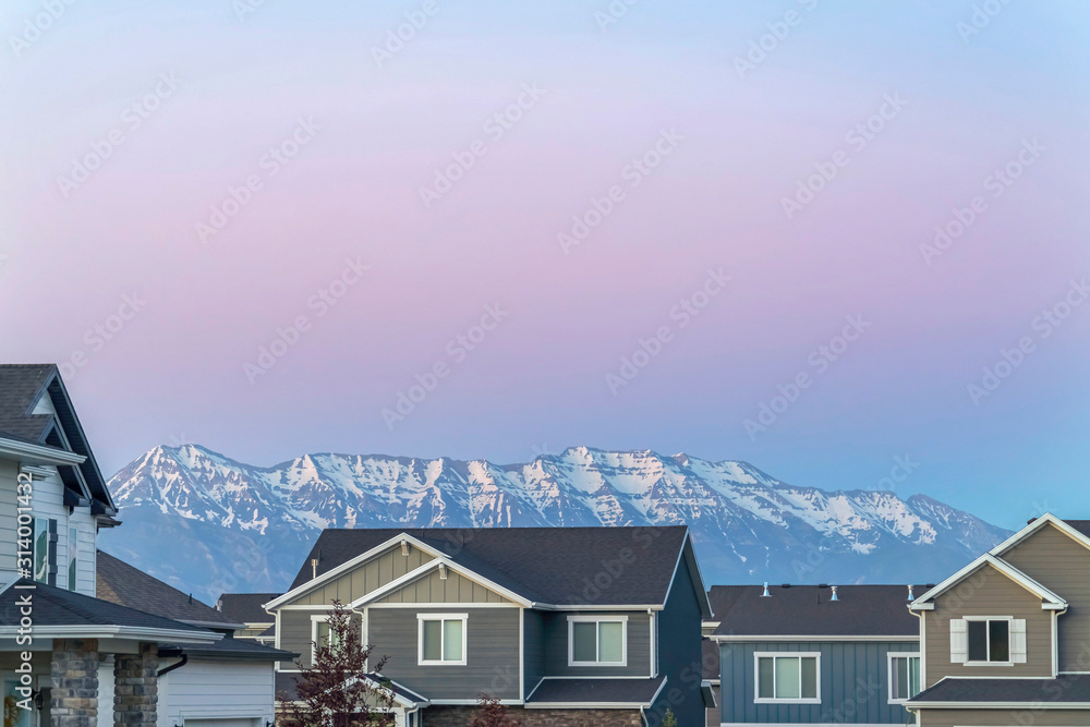 Exterior of houses with gray walls and gable roofs against snow capped mountain