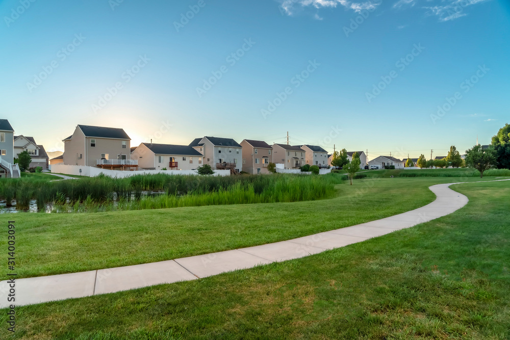 Grassy pond and pathway winding through lush green lawn with homes background Grassy pond and pathway winding through lush green lawn with homes background