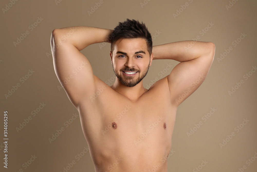 Fototapeta premium Young man showing hairless armpits after epilation procedure on brown background