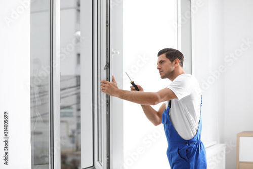 Construction worker repairing plastic window with screwdriver indoors