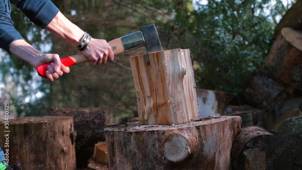 A man drives an ax with a strong blow into a wooden log.